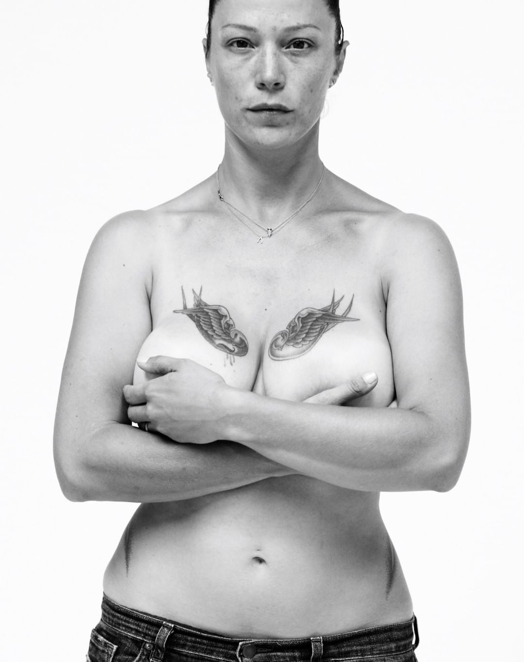 Portrait of a woman with bird chest tattoos wearing denim jeans against a white background by Koto Bolofo