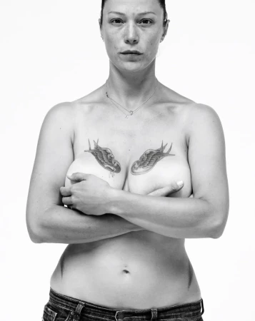 Portrait of a woman with bird chest tattoos wearing denim jeans against a white background by Koto Bolofo