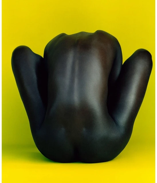 An abstract nude photography of a person with a dark skin tone in a seated position against a vivid yellow backdrop.