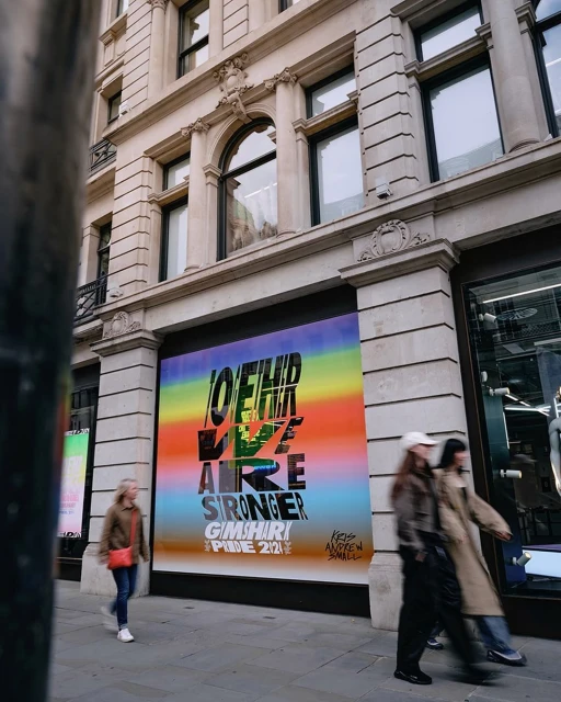 Outdoor shot of people walking past a building with a large advertisement featuring a rainbow gradient and bold black text.