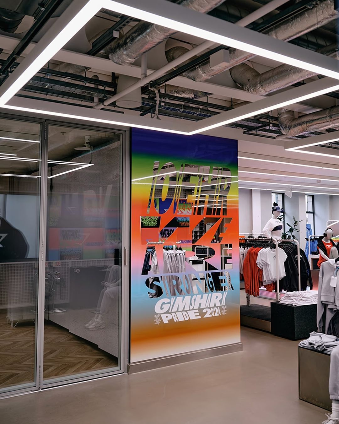 Interior view of a retail store with a large graphic display featuring a rainbow gradient and bold typography, showcasing the Pride 2021 collection.