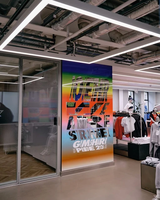 Interior view of a retail store with a large graphic display featuring a rainbow gradient and bold typography, showcasing the Pride 2021 collection.