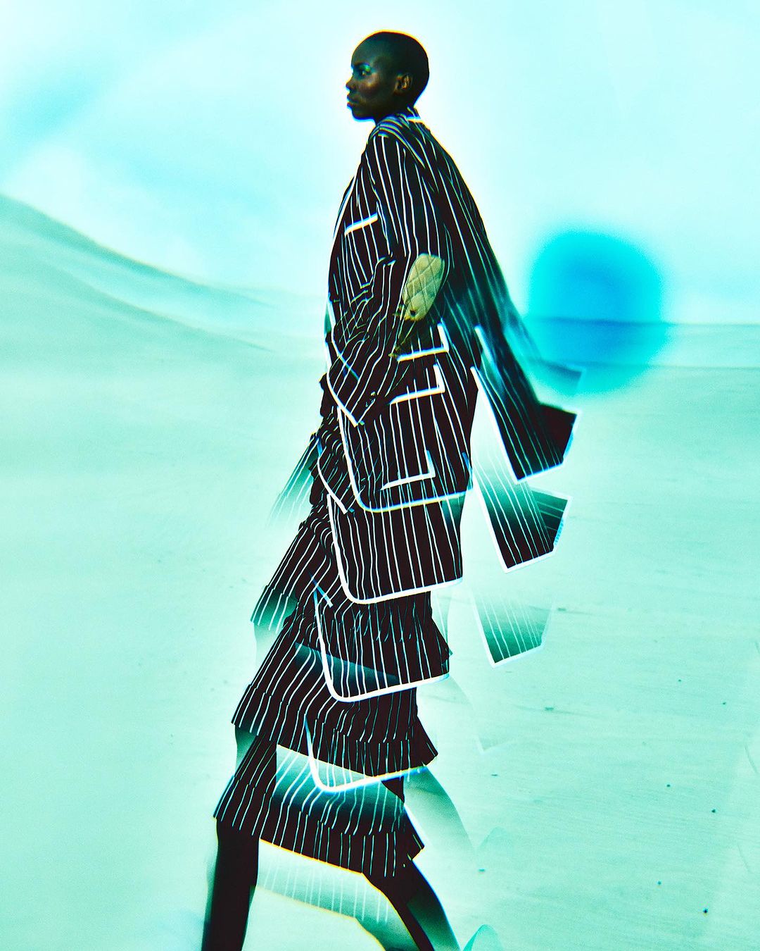 Woman in striped blazer and skirt walking against an abstract blue background in a fashion editorial with motion blur and light effects.