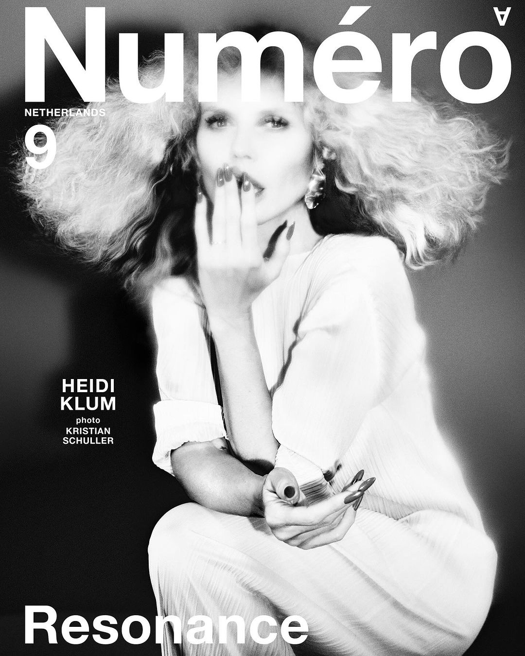 Black and white magazine cover featuring Heidi Klum with curly blonde hair and manicured nails, wearing a white outfit, with dramatic lighting.