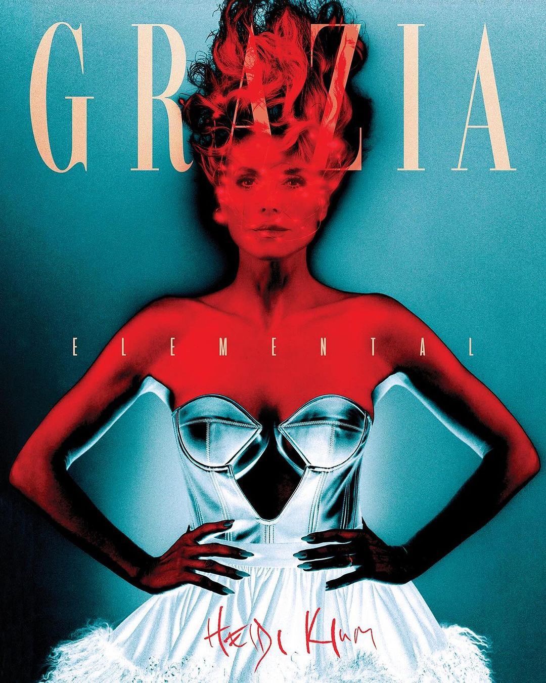 Woman with red hair and silver bustier on GRAZIA magazine cover. Red face effect, white tutu skirt, blue backdrop. Fashion editorial.