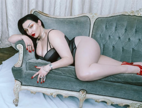 Woman in black lingerie and red heels lying on an ornate green velvet sofa, photographed by Kristin-lee Moolman