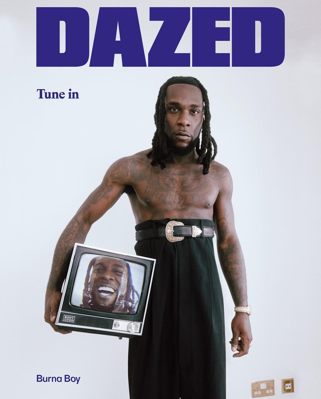 Portrait of Burna Boy on Dazed magazine cover, holding a vintage TV with his image on screen, against a plain white background.