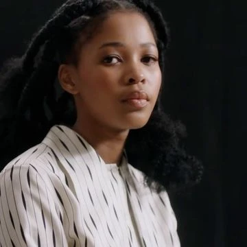 Portrait of a black woman with dark braided hair wearing a white and black striped top against a dark background