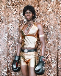 Portrait of a man in metallic gold top and shorts wearing black boxing gloves against a leopard print backdrop