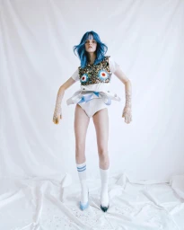 Model with vibrant blue hair wearing embellished white top and socks photographed against white backdrop by Kristin-lee Moolman