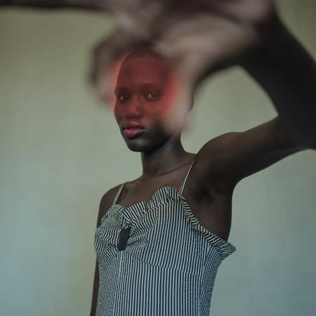 Portrait of a bald Black woman in a striped camisole with a hand reaching toward the camera against a plain background