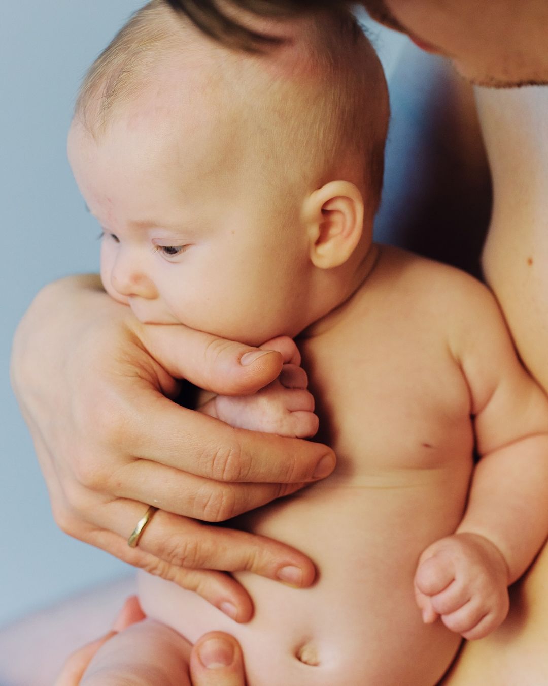 Close-up portrait of an infant being held gently by an adult, with soft natural light and a clean background.