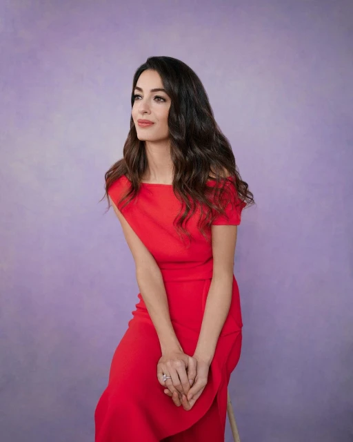 Adult woman in red dress with shoulderless detail sitting in a photo studio with a purple background looking towards the left.