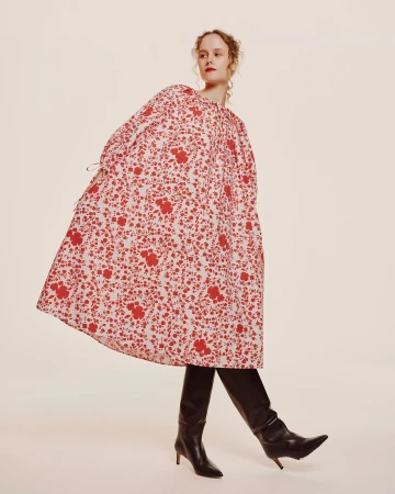Model in voluminous red and white floral dress wearing black leather boots against a white studio background