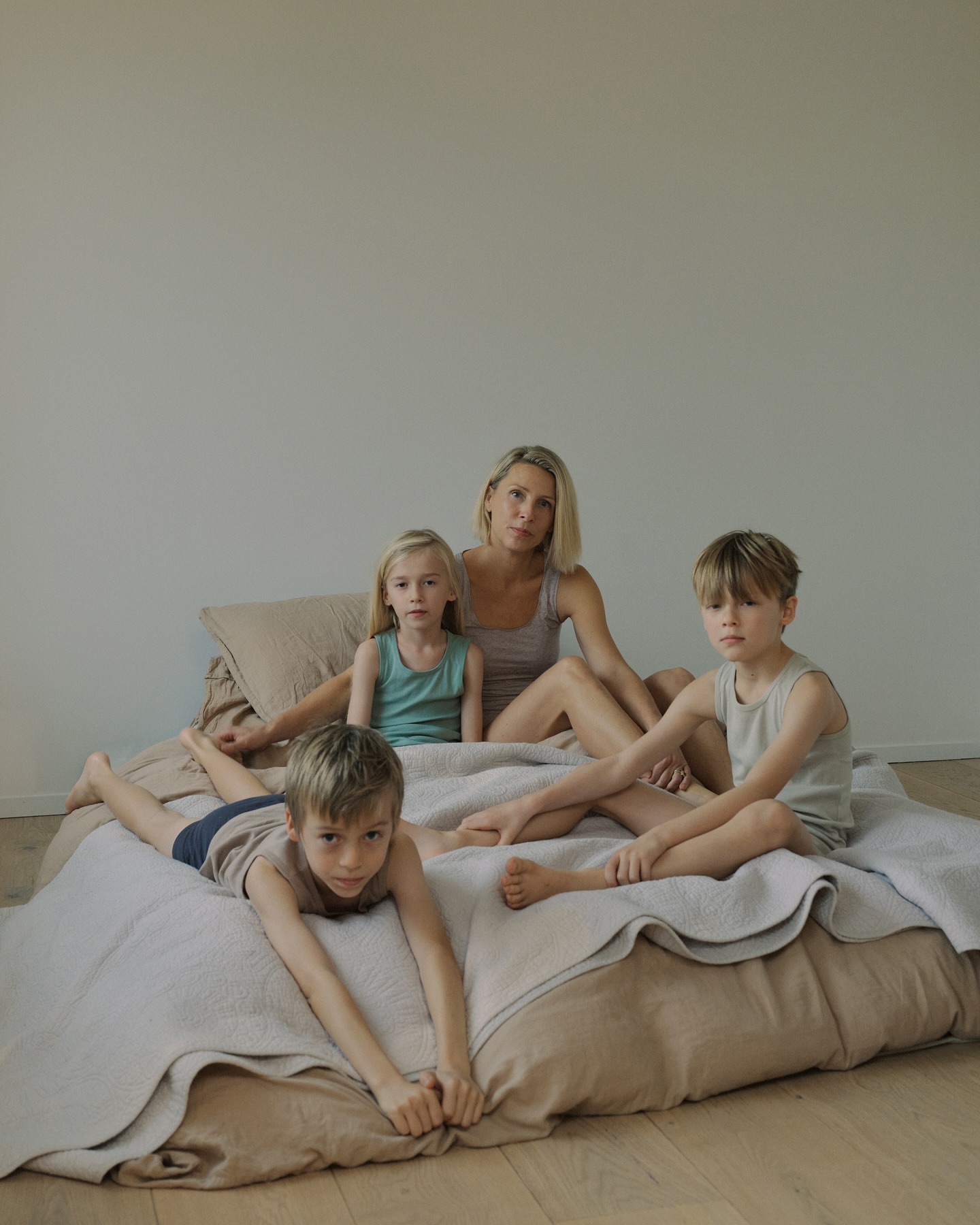 A mother with her three children are sitting on a bed. They are dressed in casual clothes, posing for a family portrait.