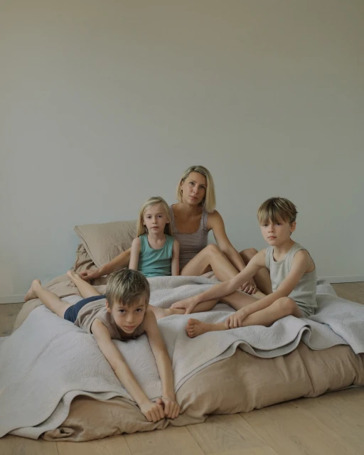A mother with her three children are sitting on a bed. They are dressed in casual clothes, posing for a family portrait.