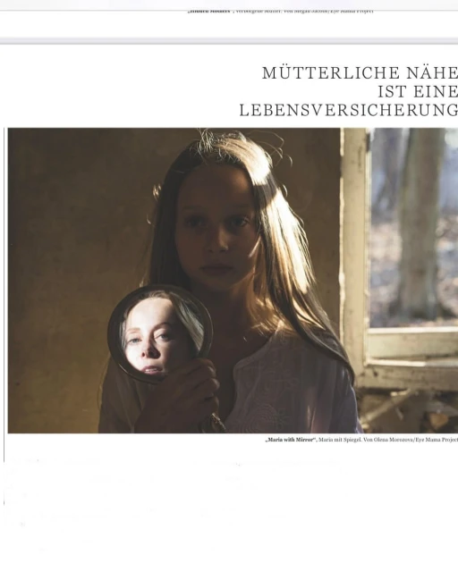 Young woman holds a mirror reflecting her face indoors, with window light and neutral tones creating a contemplative atmosphere.
