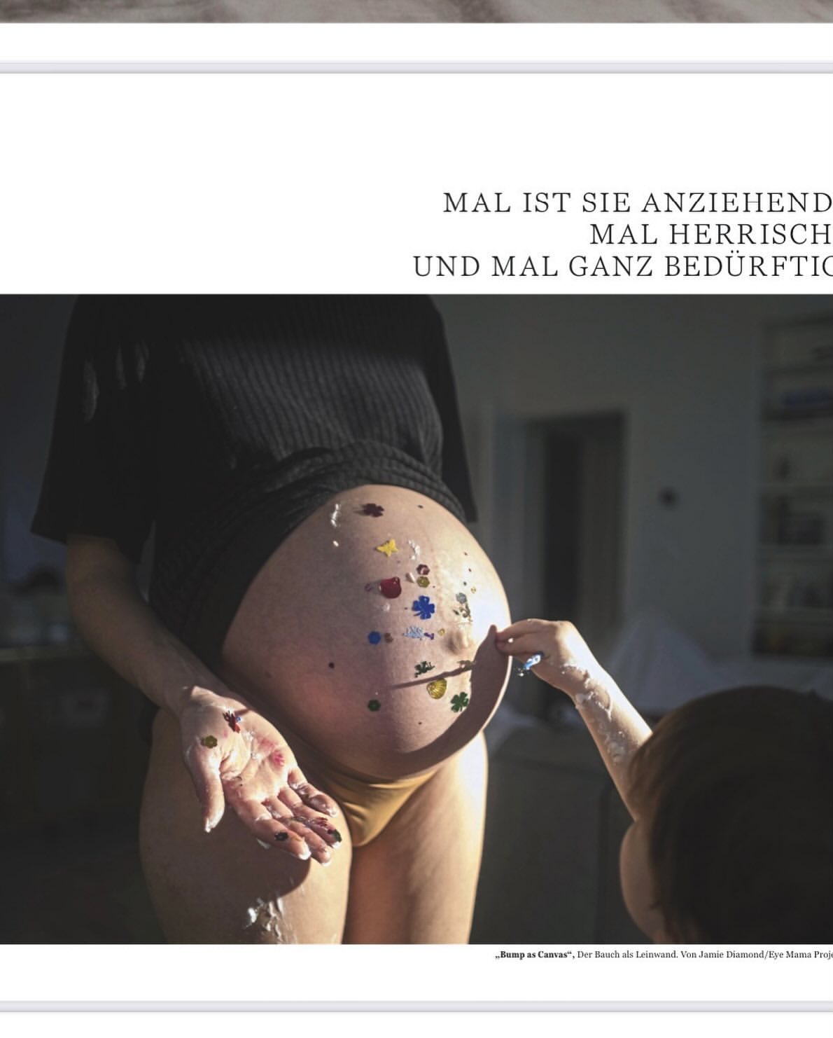 Pregnant adult female with belly art showing flower designs being touched by a child's hand in an indoor environment.