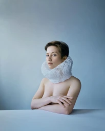 Portrait of a woman wearing a white knitted neck ruff against a pale blue background photographed by Kristina Varaksina