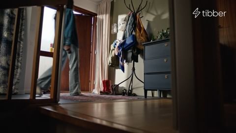 Person entering an entryway with wood floors, a blue dresser, and a coat rack in a softly lit home interior.