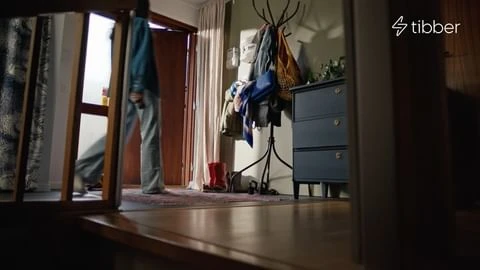 Person walking through a doorway into a domestic hallway with a dark blue chest of drawers and coat rack.