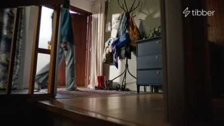 Person walking through a doorway into a domestic hallway with a dark blue chest of drawers and coat rack.