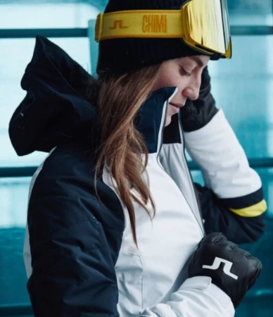 Woman in ski jacket adjusting zipper, wearing black beanie, yellow goggles and gloves by Kristofer Samuelsson