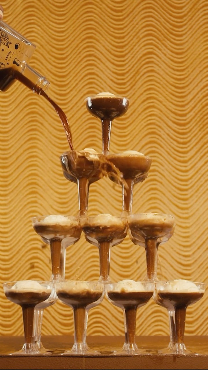 Champagne tower creation with clear coupe glasses filled with white ice cream and brown liquid in a warm-toned, indoor setting.