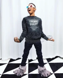 Young boy wearing 3D glasses, graphic sweatshirt, and fuzzy slippers holding spring toys on white backdrop