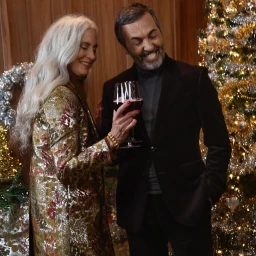 An older man and woman celebrating with wine glasses next to a decorated Christmas tree in New York by Kristyna Archer.