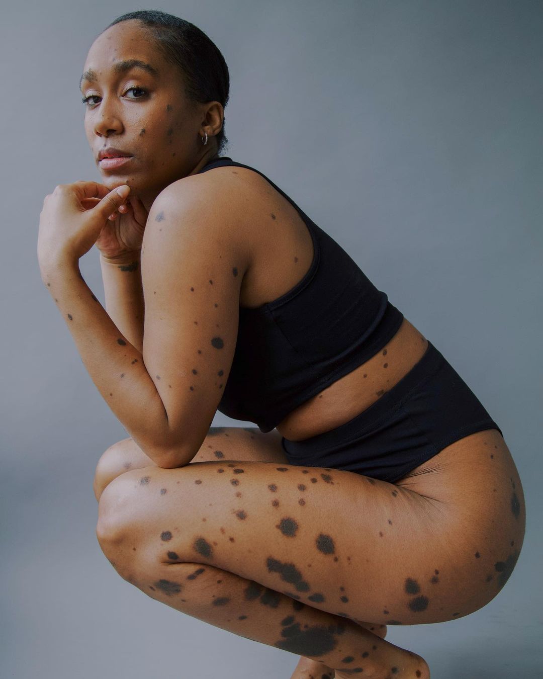 Woman in black activewear crouching in a studio setting with fair lighting, showcasing athletic fashion and body positivity.