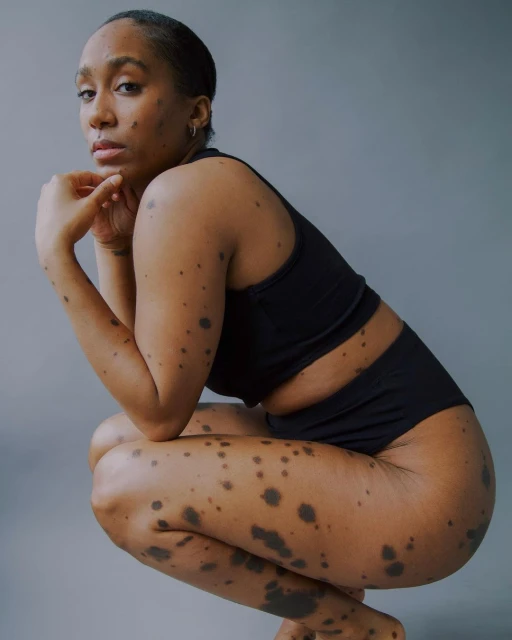Woman in black activewear crouching in a studio setting with fair lighting, showcasing athletic fashion and body positivity.