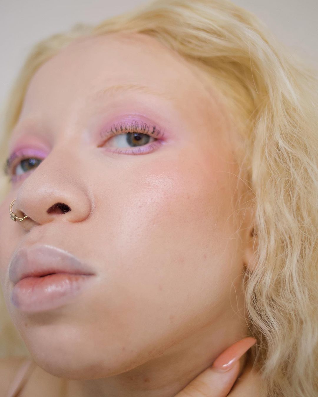 Close-up portrait of a woman with albinism wearing pink eye makeup, showcasing beauty and fashion details in a soft light.