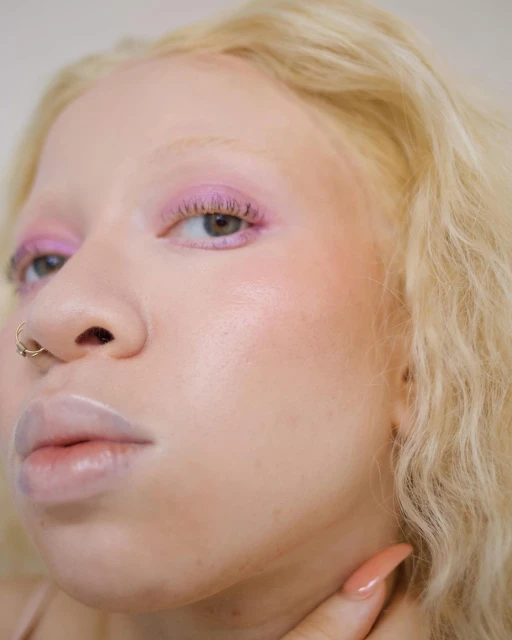 Close-up portrait of a woman with albinism wearing pink eye makeup, showcasing beauty and fashion details in a soft light.