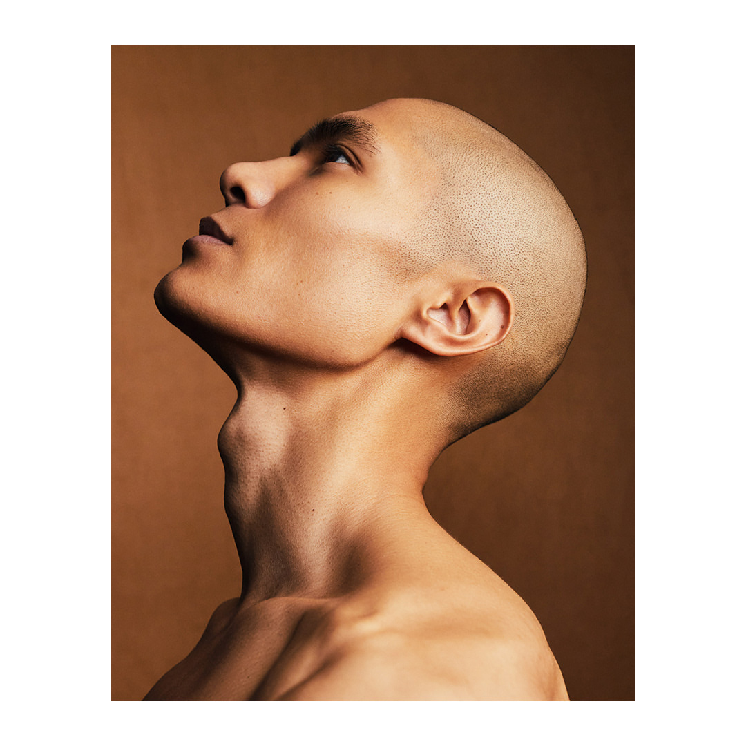 Portrait of a shaved-head adult male looking up against a monochrome brown background in a studio setting with shallow depth of field.
