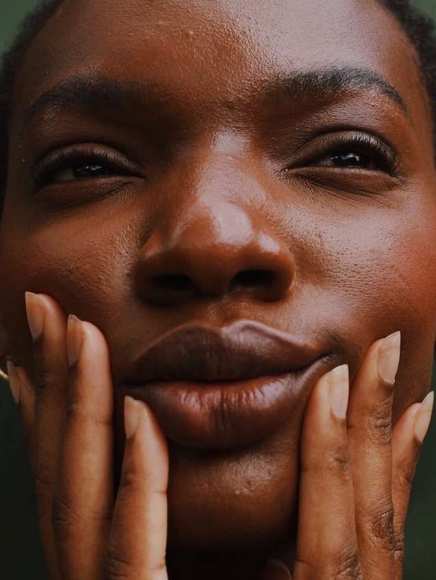 Close-up portrait of an adult Black female with hands touching her cheeks, creating a symmetrical and intimate facial focus.