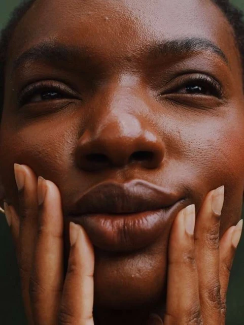 Close-up portrait of an adult Black female with hands touching her cheeks, creating a symmetrical and intimate facial focus.