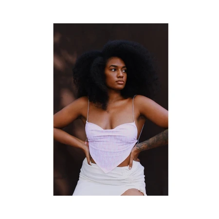 Black woman with voluminous dark hair wearing a light pink halter top and white skirt against a dark background