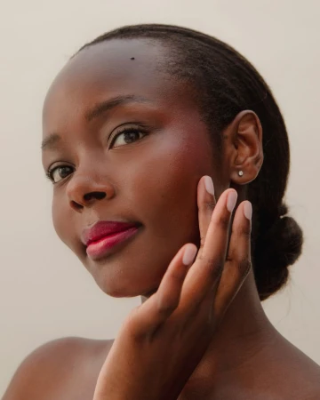 Close-up portrait of a Black woman with dark hair tied back, touching her cheek against a neutral light background.