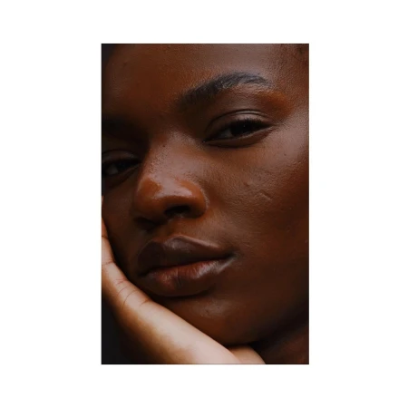 Close-up portrait of a Black woman resting her face on her hand with natural lighting.
