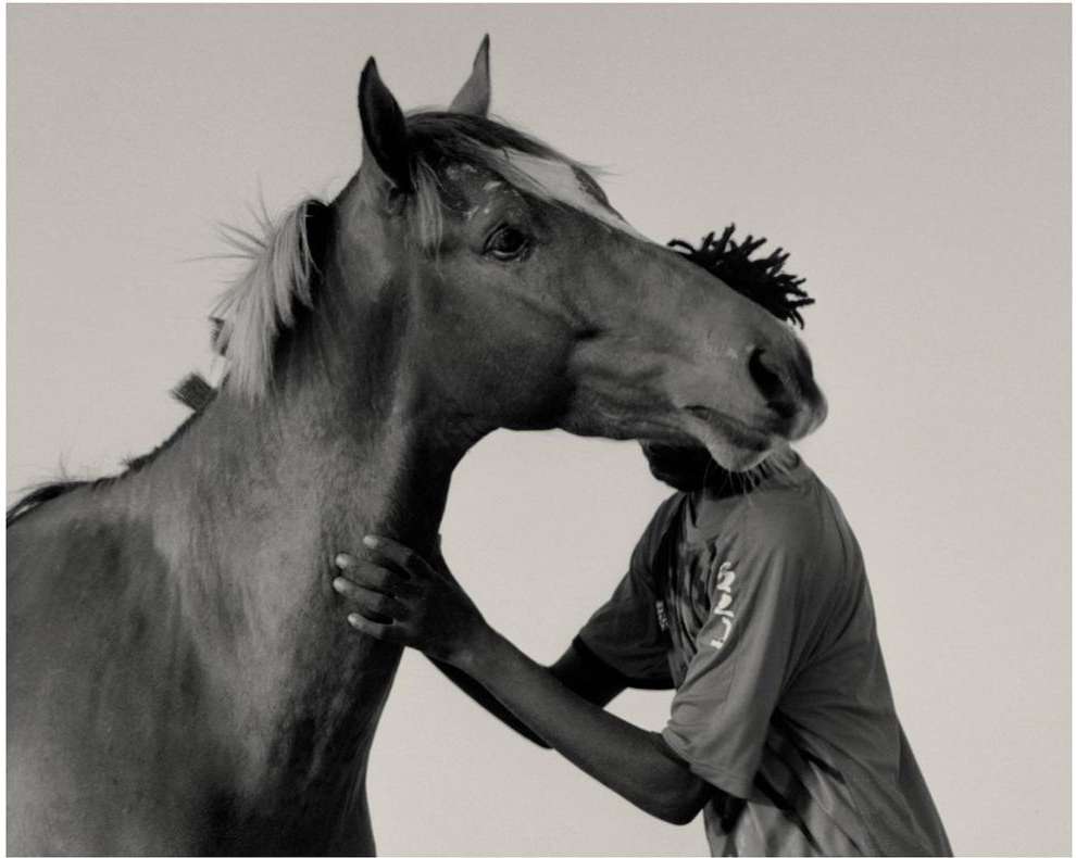 Black man standing beside a horse against a plain light background photographed by Kwabena Sekyi Appiah-nti