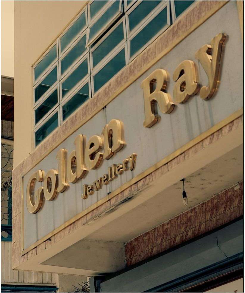 Storefront sign for Golden Ray Jewellery with gold lettering and a window bank above. Building exterior with a commercial sign.