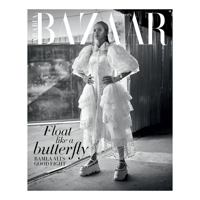 Black and white magazine cover featuring a woman in a white dress and platform shoes, standing against an industrial backdrop.
