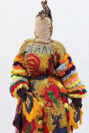 Full-length studio shot of an individual wearing a colorful, ornate costume with animal motifs and beaded details against a white backdrop.