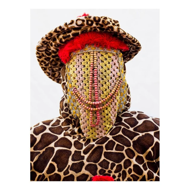 Person wearing a unique fashion ensemble featuring a leopard print hat and giraffe print body covering, with a beaded and crocheted face mask.