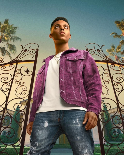 A young Black man confidently poses in front of an ornate gate and a mansion, wearing a purple jacket and ripped jeans.