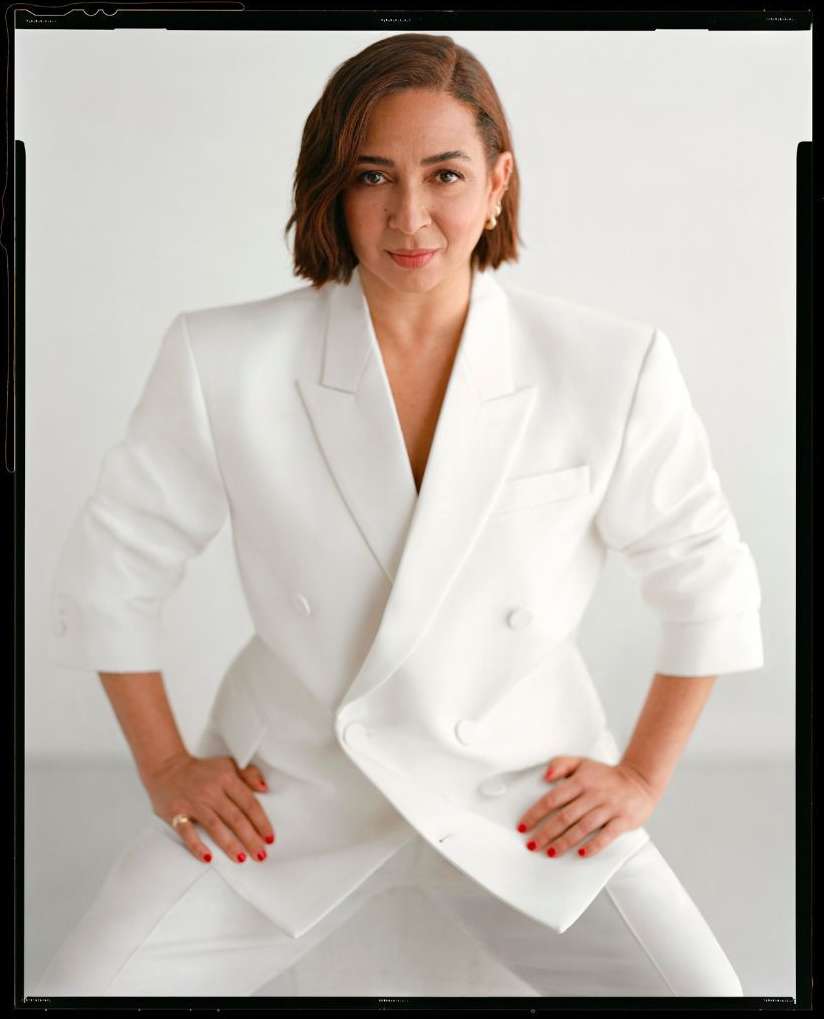 Stylish adult woman in a white pantsuit poses in front of a white backdrop in a fashion portrait with a medium studio shot.