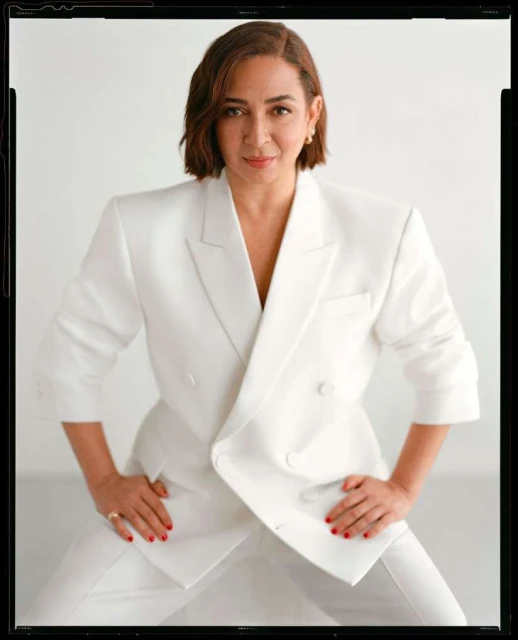Stylish adult woman in a white pantsuit poses in front of a white backdrop in a fashion portrait with a medium studio shot.