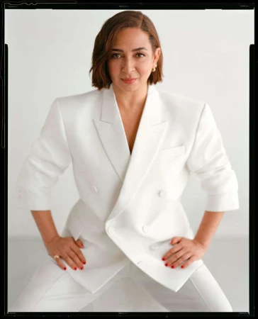 Stylish adult woman in a white pantsuit poses in front of a white backdrop in a fashion portrait with a medium studio shot.