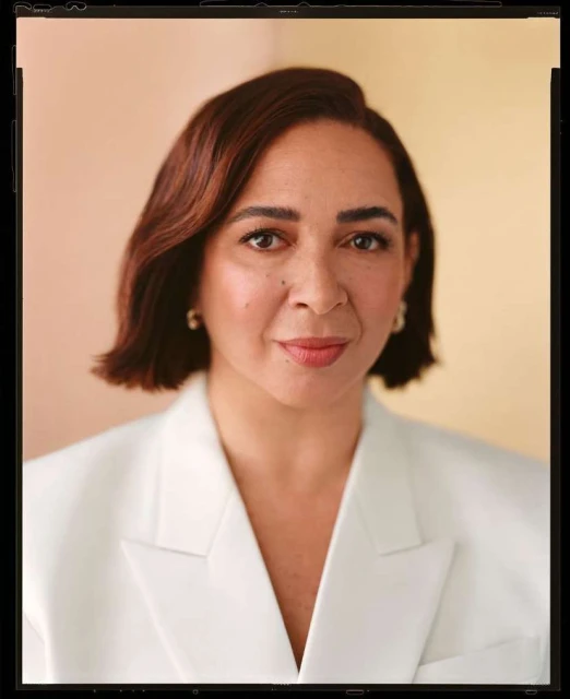 Portrait of an adult woman with brown hair in a white blazer against a softly colored background, photographed with eye-level framing.